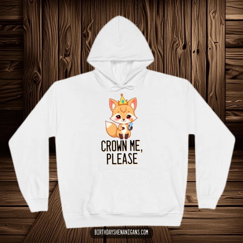 Funny fox character in a party crown holding a twinkling birthday candle, a cozy and humorous hoodie for celebrations.