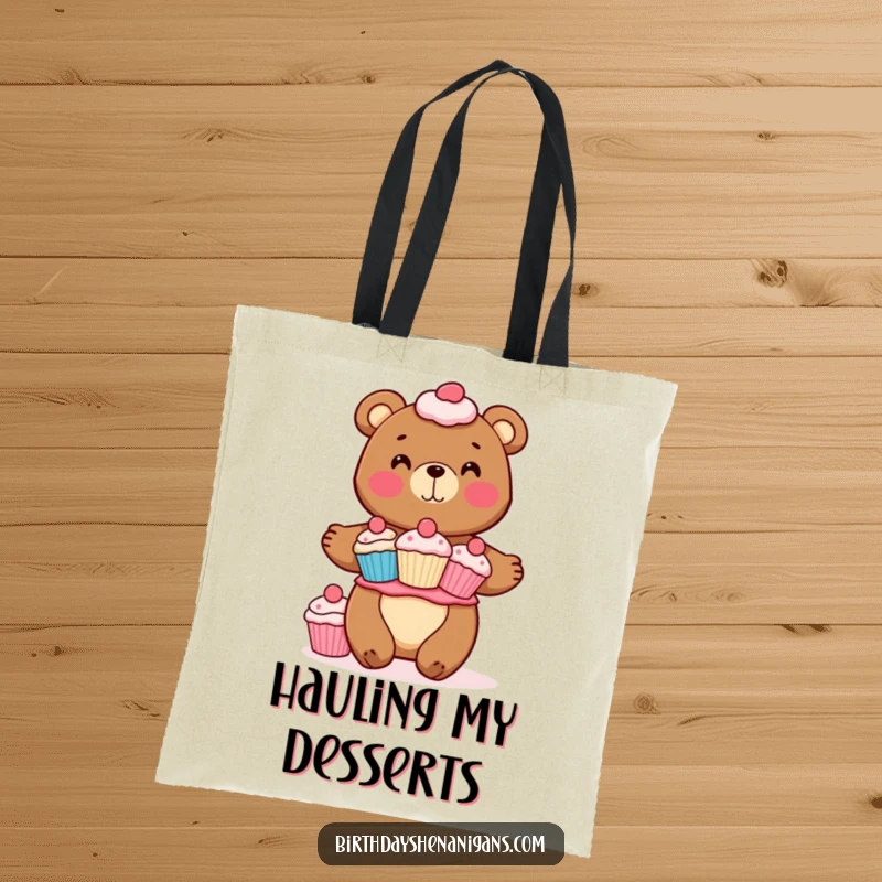 Funny tote bag showcasing a cheerful bear character precariously balancing a large stack of assorted cupcakes. A delightful accessory for treat lovers.