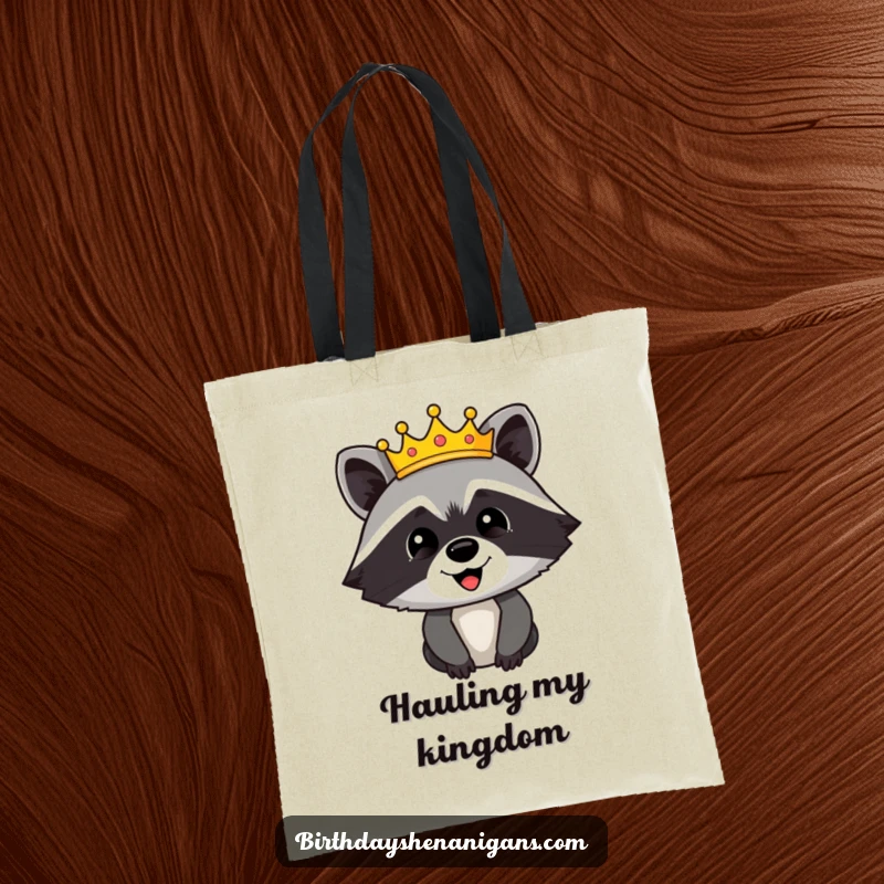 Funny tote bag featuring a happy raccoon character adorned with a festive crown, looking regal and ready for any quest.